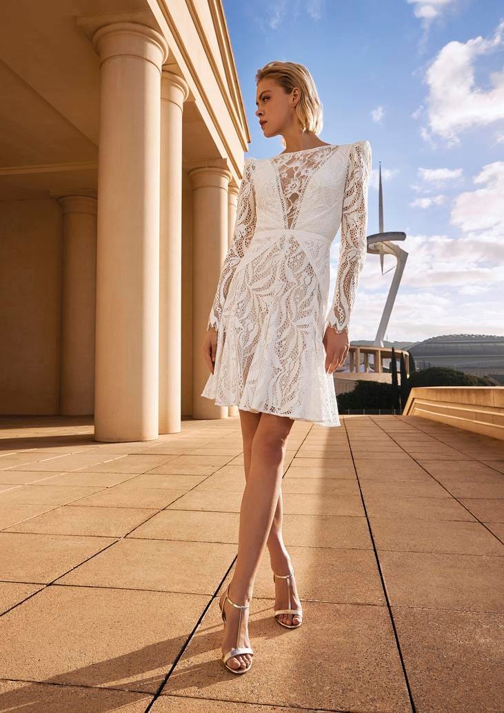 Noiva a usar um vestido acima do joelho com mangas longas e umas sandálias de salto alto
