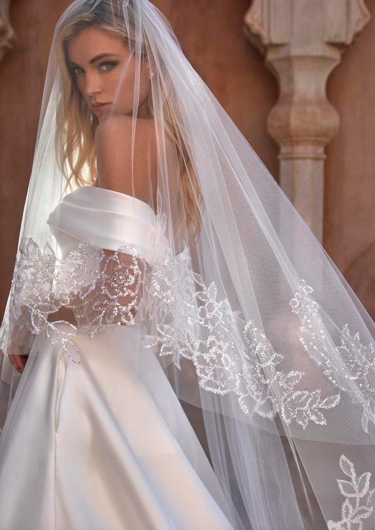 Blonde woman in a white lace bridal veil with leaf motifs detailing the edges