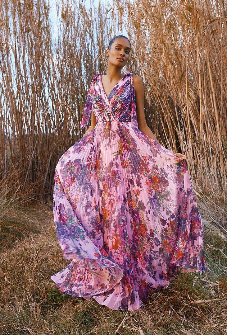 Une demoiselle d'honneur porte une longue robe rose sans manches &agrave; motif floral. La jupe fluide affiche un fini pliss&eacute;.