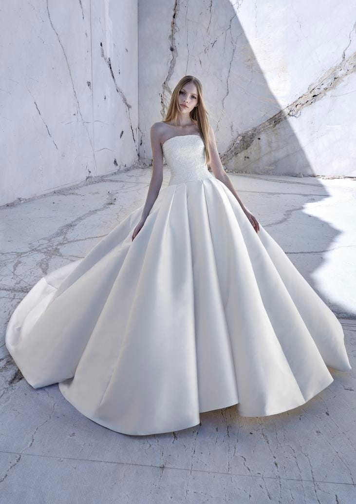 Noiva com vestido cai cai simples de cetim corte princesa, com cabelos loiros compridos, posa em cenário de mármore.