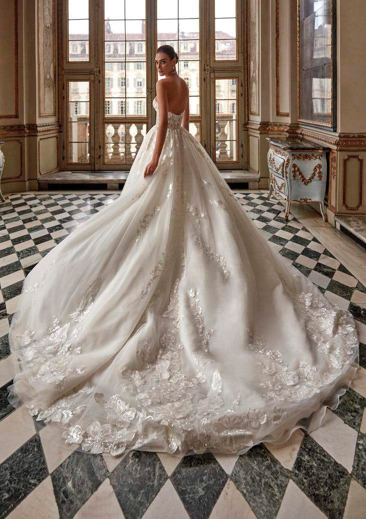 Noiva posando junto de uma janela com um vestido princesa rodado com uma causa adornada com bordados