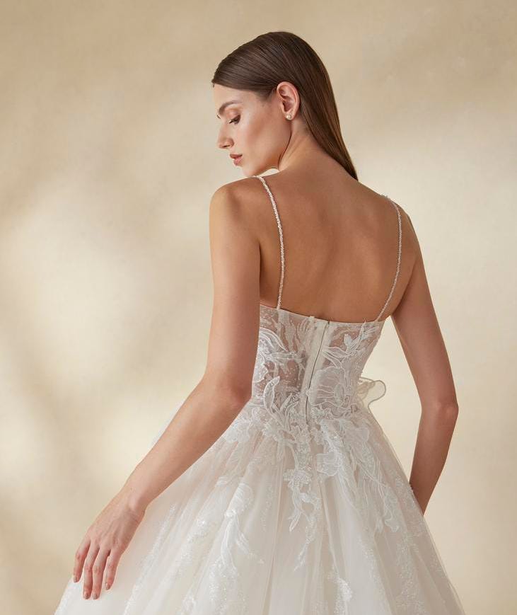 Νύφη που κοιτά το νυφικό της από το πλάι Κομψή γυναίκα που φοράει ένα νυφικό με τιράντες και φλοραλ δαντελωτά μοτίβα και κοιτάει στο πλάι