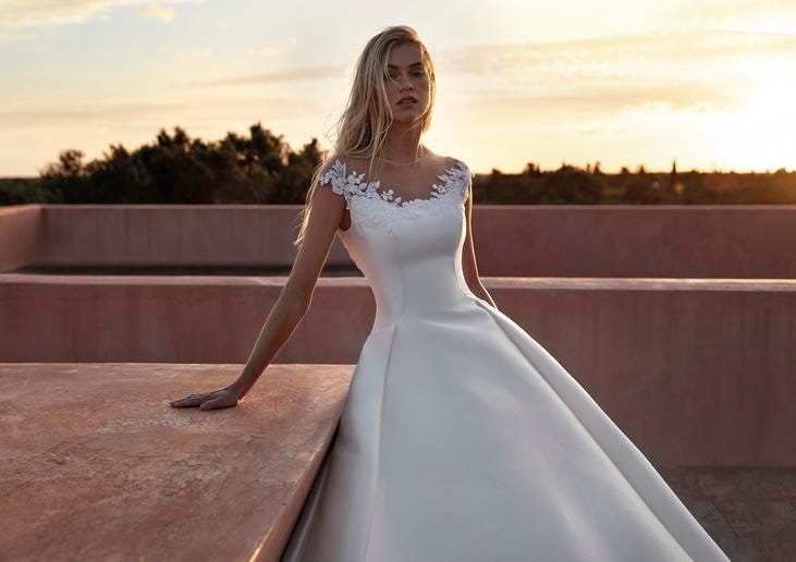 Scoop neck wedding dress Blonde-haired woman wearing a scoop-neck wedding dress with short sleeves and floral detailing lining the neckline.