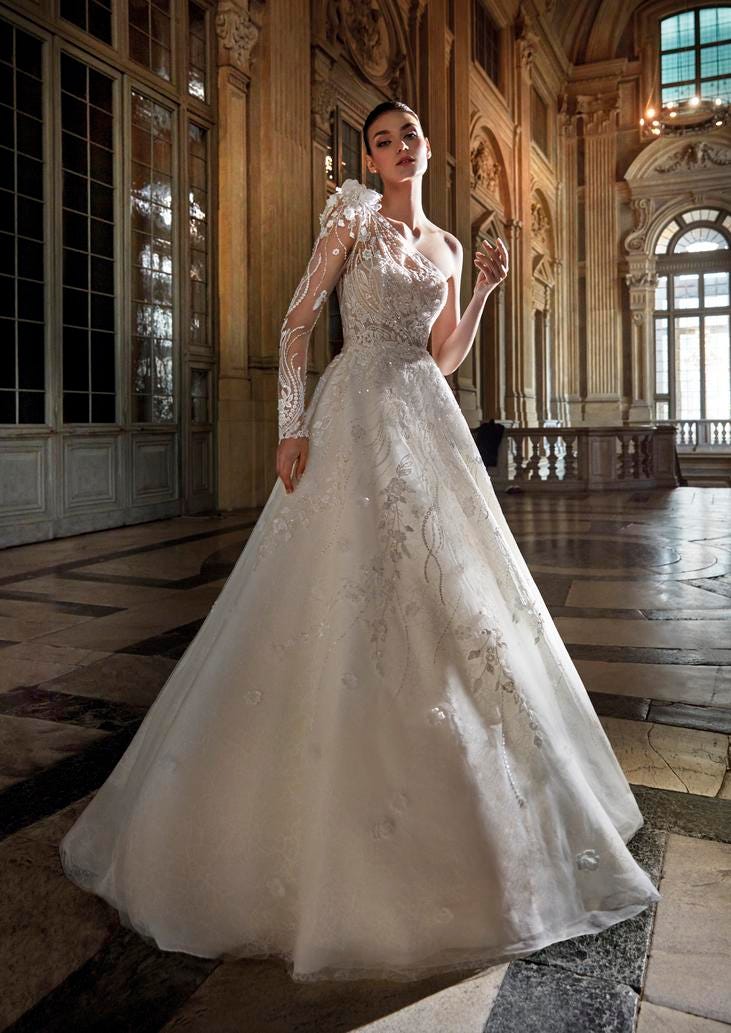 Abito Sposa Lungo Monospalla Modella che indossa un lungo abito da sposa monospalla con manica lunga decorato
