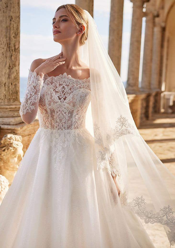 Une mari&eacute;e resplendissante dans une robe de mari&eacute;e bustier &agrave; manches longues. Le bustier transparent est orn&eacute; de dentelle