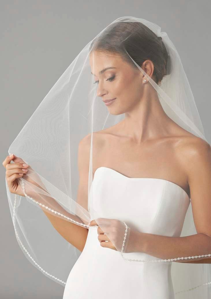 Mujer llevando un velo de princesa de novia y mir&aacute;ndolo mientras lo toca
