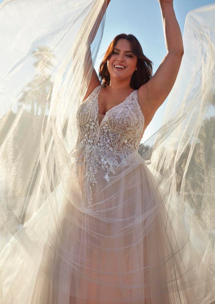 Mujer con vestido de novia plus size sujetando su velo ri&eacute;ndose con un vestido amp&oacute;n de tul