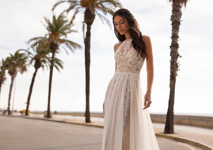 Kobieta z ciemnymi włosami i zamkniętymi oczami prezentująca koronkową suknię ślubną na tle palm