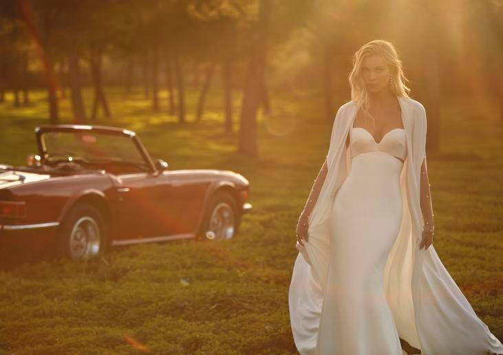 Noiva posa ao entardecer com vestido corte sereia simples longo, com casaco de noiva e cabelos soltos com brincos