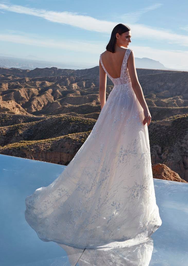Modella di spalle che indossa un lungo abito da sposa ricamato in pizzo con scollatura sulla schiena.