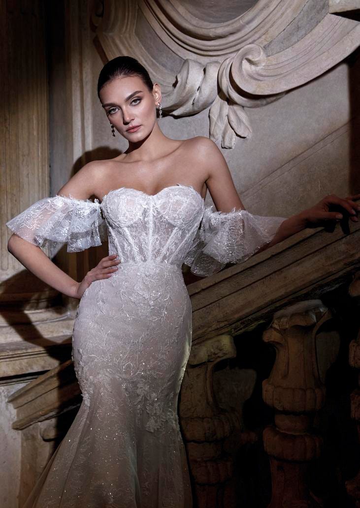 Jeune mariée habillée d’une robe de mariée décolleté cœur à manches courtes, s'appuyant sur une barre d’escaliers en pierre.