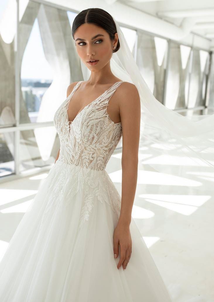 Noiva usando um vestido de alças princesa com um decote em bico adornado com detalhes rendados e conjugado com um véu