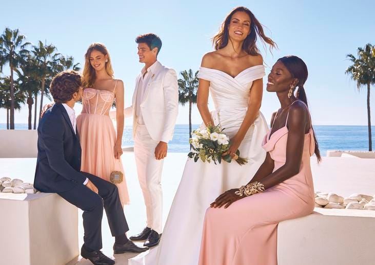 Woman in V-neck off-the-shoulder wedding dress holding a bouquet standing next to woman in pink bridesmaid dress