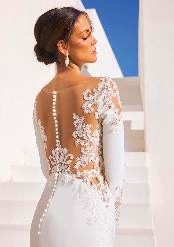 Modella che indossa un abito da sposa a sirena a maniche lunghe in crepe e pizzo in sovrapposizione.