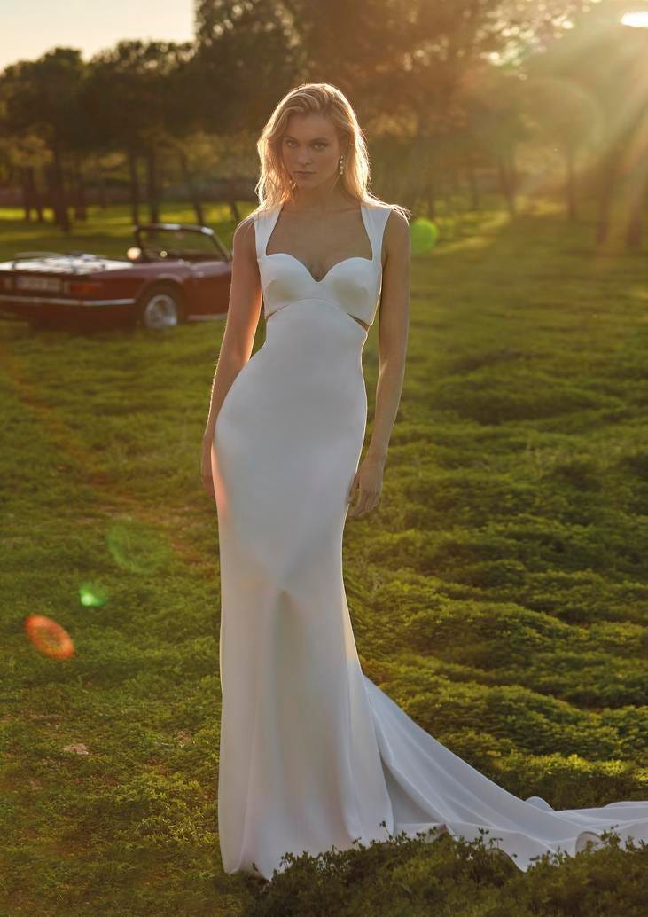 Blonde woman in simple A-line wedding dress with sweetheart neckline standing in front of a classic red car