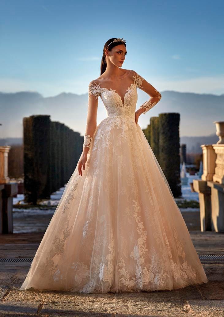 Une robe de mari&eacute;e luxueuse &agrave; manches longues, con&ccedil;ue avec de la dentelle et du tulle, &eacute;voquant l'&eacute;l&eacute;gance et la gr&acirc;ce.