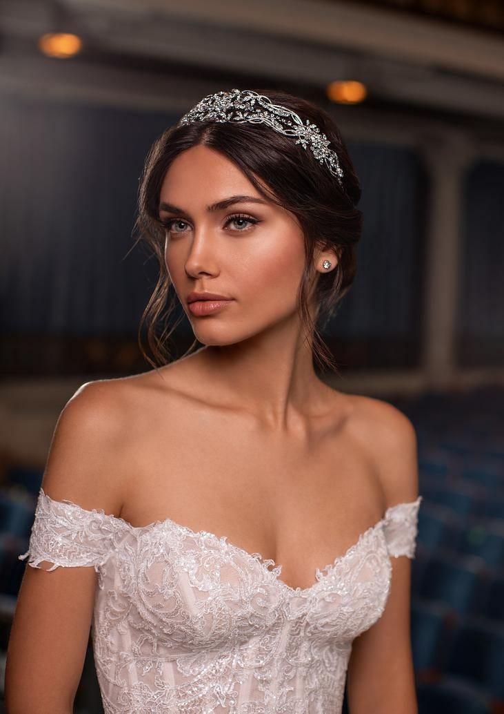 Donna con trucco da sposa naturale, orecchini semplici e coroncina. Indossa un vestito da sposa con spalle scoperte