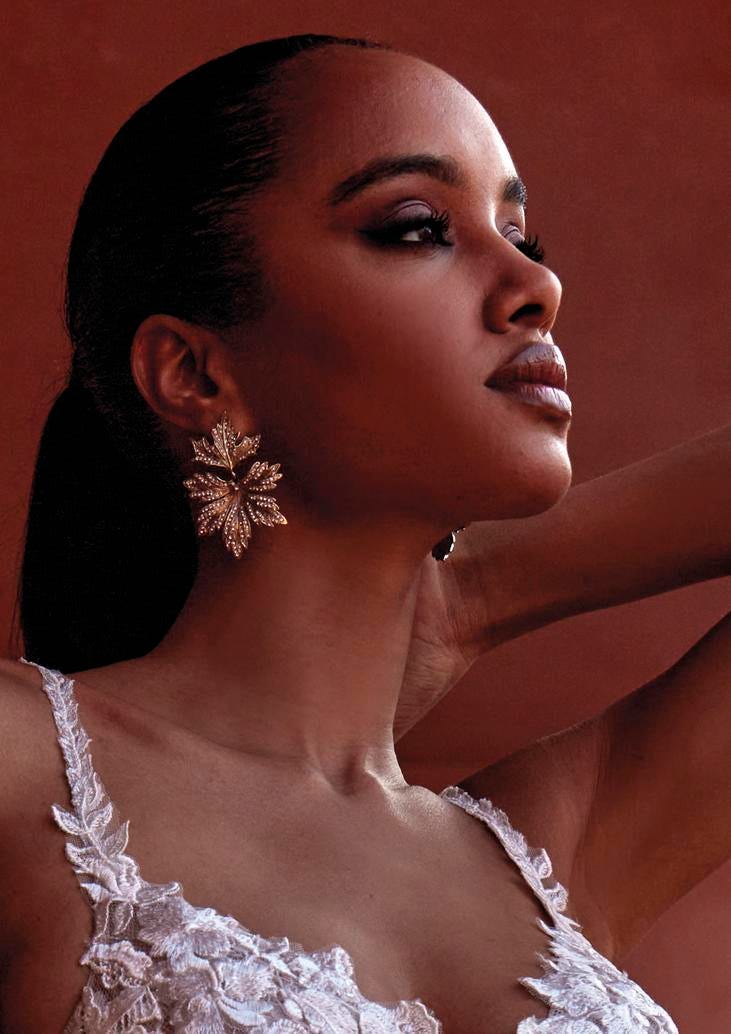 Vestido de noiva de alças Noiva usando uns brincos em forma de folha na cor dourada, combinado com um penteado rabo de cavalo e make em tons escuros