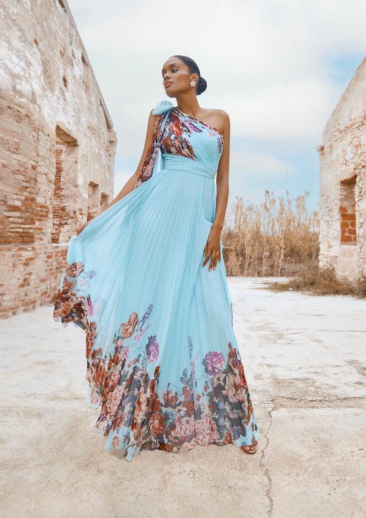 Woman with dark hair in a low bun wearing a one-shouldered, light blue formal gown with floral details