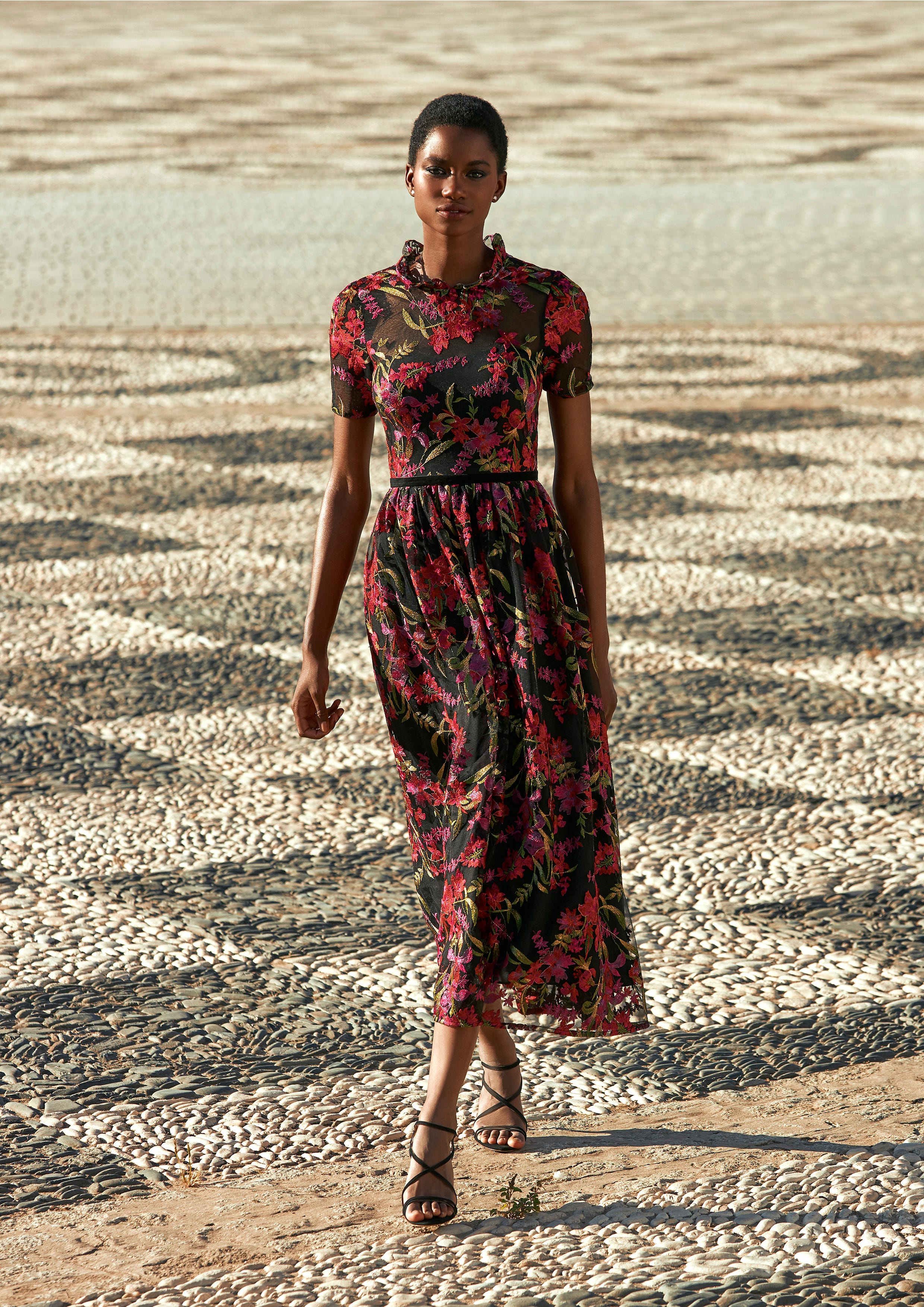 Una mujer con el pelo corto al aire libre luciendo un vestido para madre de la novia negro con estamapado de flores.