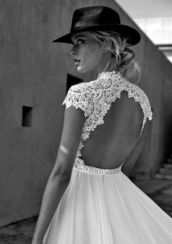Ein Schwarz-Weiß Foto von einer Frau mit hochgestreckten, blonden Haaren schaut über ihre Schulter und trägt einen Cowboyhut und ein Brautkleid mit detailverziertem Rückenausschnitt. 