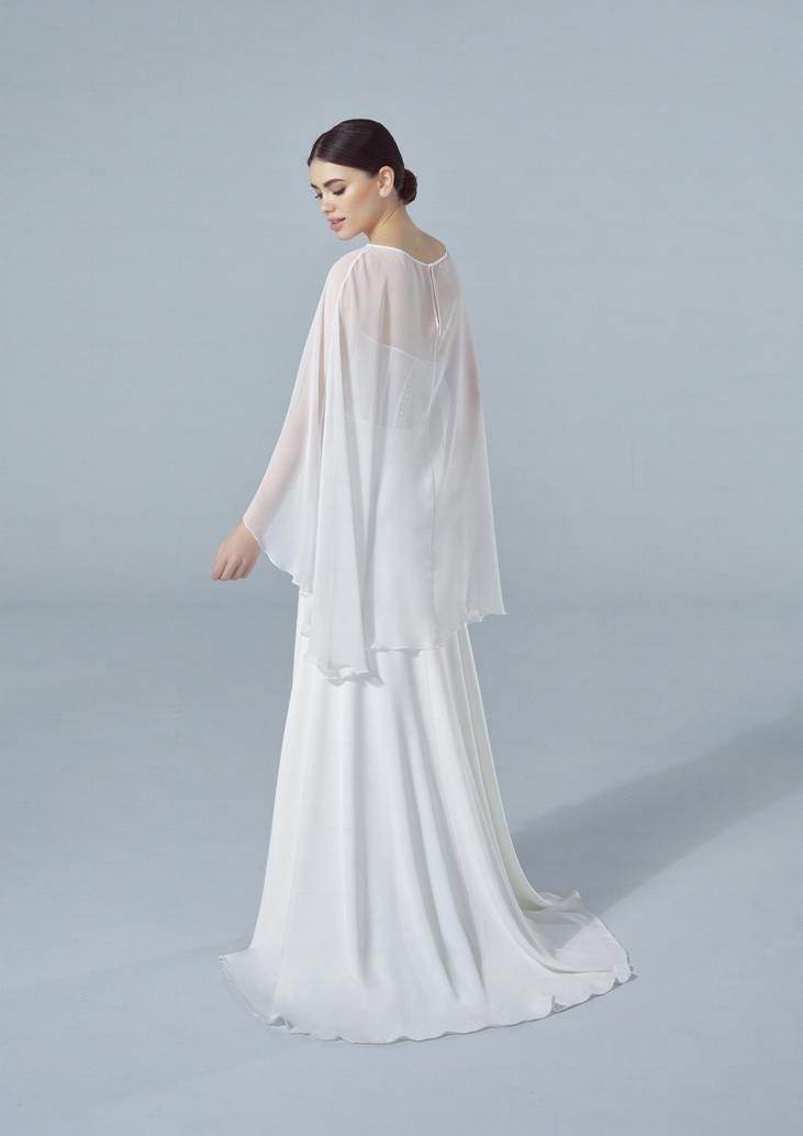 Woman in a white bridal dress, with a chiffon wedding cape, flowing gracefully behind her