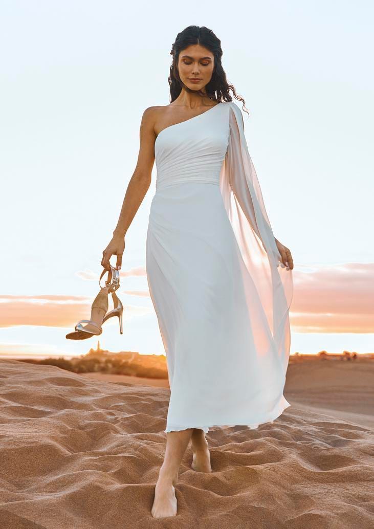White wedding heels Brunette wearing a sheath bridal dress and carrying a pair of white wedding heels, walking on the beach
