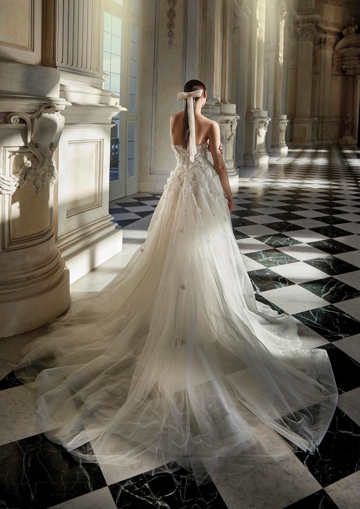 Woman with a white bow wearing a flared wedding gown with exposed back and a catherdal train inside a ballroom