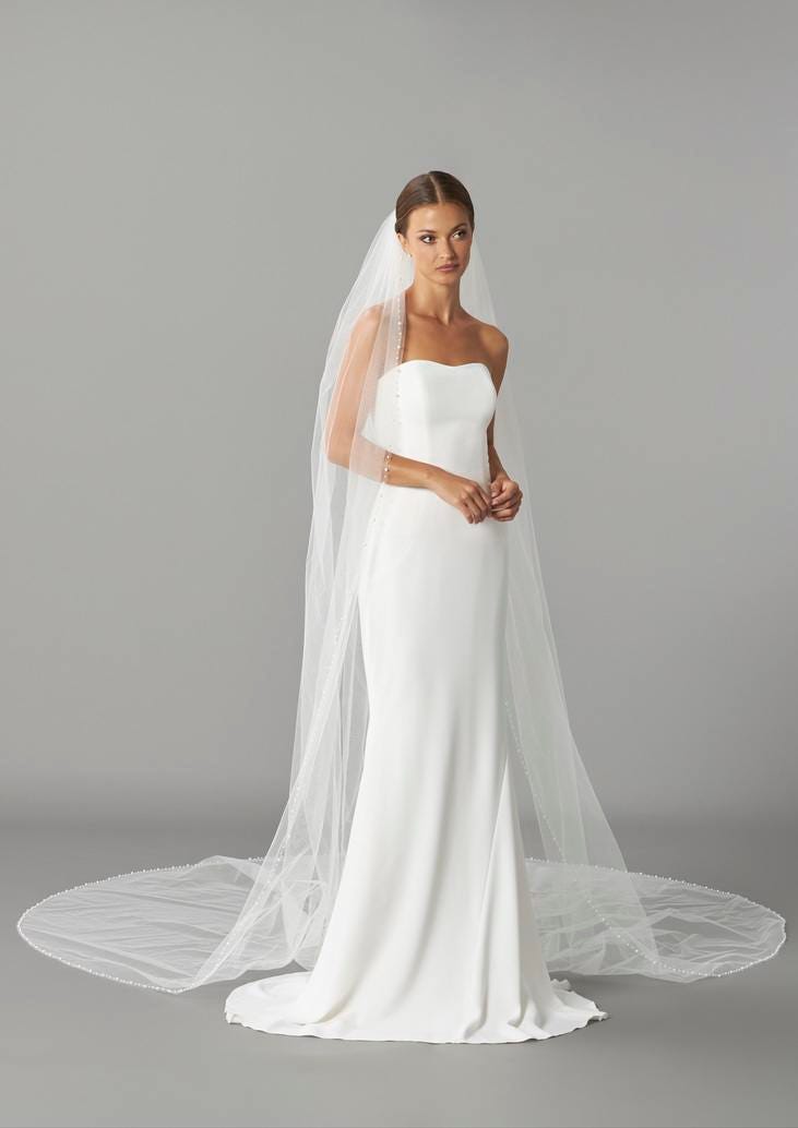 Woman wearing a strapless wedding gown and a long white bridal veil against a grey background