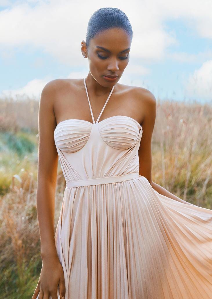 Woman wearing an A-line nude party dress with delicate straps, standing in a field