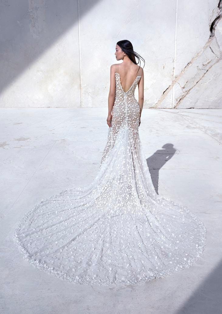 Brunette wearing a sleeveless sheath wedding dress with V-back, standing outside 
